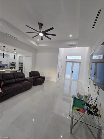 Living room with a raised ceiling, recessed lighting, french doors, and ceiling fan