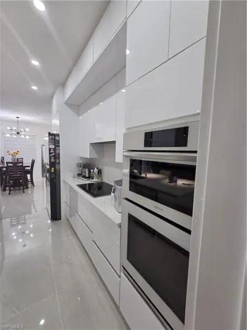 Kitchen with white cabinetry, modern cabinets, double wall oven, stovetop, and light stone countertops