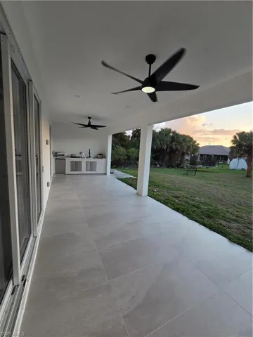 Patio terrace at dusk featuring an outdoor kitchen, a ceiling fan, a lawn, and a patio area