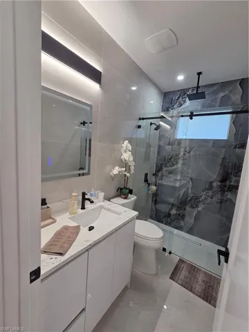 Full bath featuring vanity, tile walls, and a marble finish shower