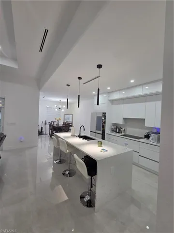 Kitchen featuring modern cabinets, white cabinets, a kitchen bar, a spacious island, and hanging light fixtures