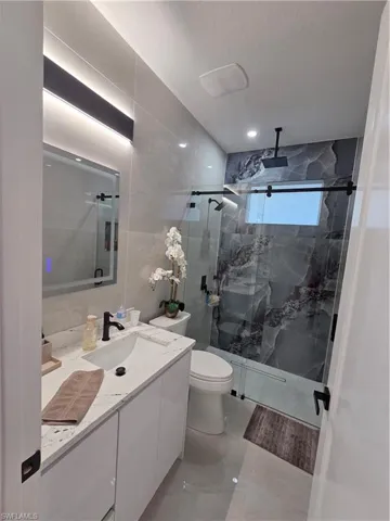 Bathroom with vanity, a marble finish shower, and tile walls