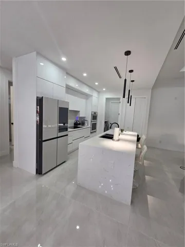 Kitchen with fridge, white cabinetry, an island with sink, modern cabinets, and light stone countertops