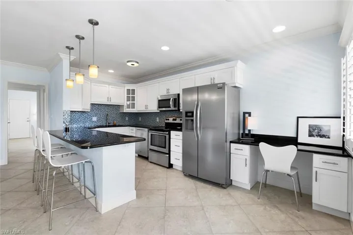 Kitchen with appliances with stainless steel finishes, decorative backsplash, white cabinets, a breakfast bar area, and pendant lighting