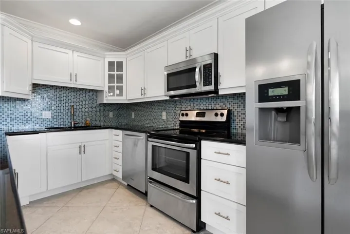 Kitchen with white cabinets, light tile patterned flooring, sink, tasteful backsplash, and appliances with stainless steel finishes