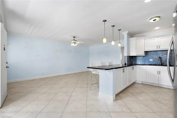 Kitchen featuring pendant lighting, white cabinets, ornamental molding, sink, and kitchen peninsula