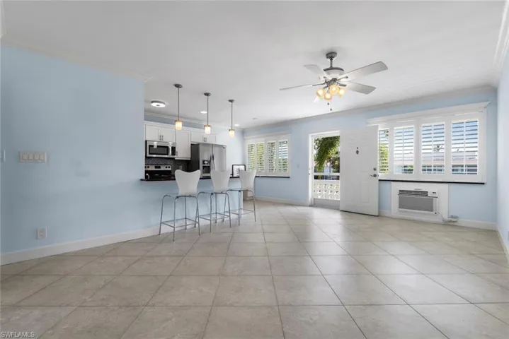 Living room with ornamental molding, ceiling fan, a wall mounted air conditioner, and a wealth of natural light