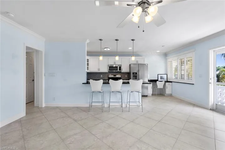 Kitchen with hanging light fixtures, white cabinetry, appliances with stainless steel finishes, a kitchen breakfast bar, and crown molding
