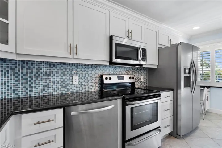 Kitchen featuring white cabinets, light tile patterned floors, ornamental molding, appliances with stainless steel finishes, and decorative backsplash