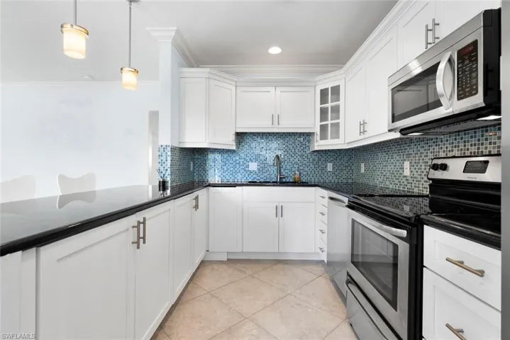 Kitchen with decorative light fixtures, stainless steel appliances, sink, and white cabinetry
