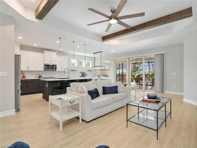 Open-concept living space featuring wood-finish flooring, a tray ceiling with exposed beams, and a ceiling fan