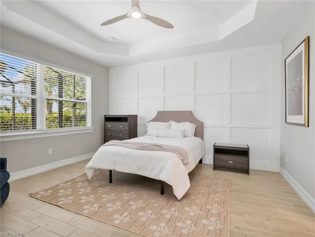 Tray ceiling with a modern ceiling fan, board and batten accent wall, large window with blinds, and light wood-finish flooring