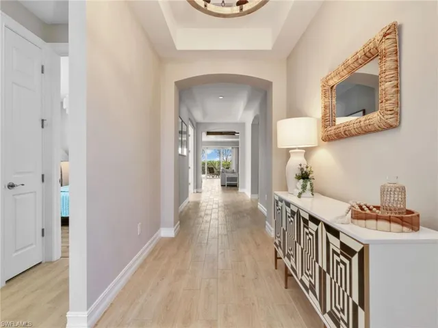 Hallway featuring wood-finish flooring, an arched entryway, and tray ceiling detail