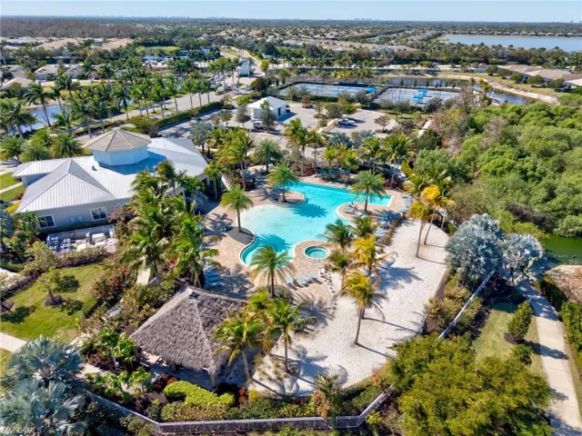 Expansive community area featuring a large freeform swimming pool with integrated spa, multiple palm trees, and a thatched-roof cabana