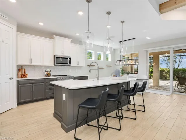 Kitchen featuring a two-tone cabinetry design, white countertops, stainless steel appliances, a center island with pendant lighting, and wood-finish flooring