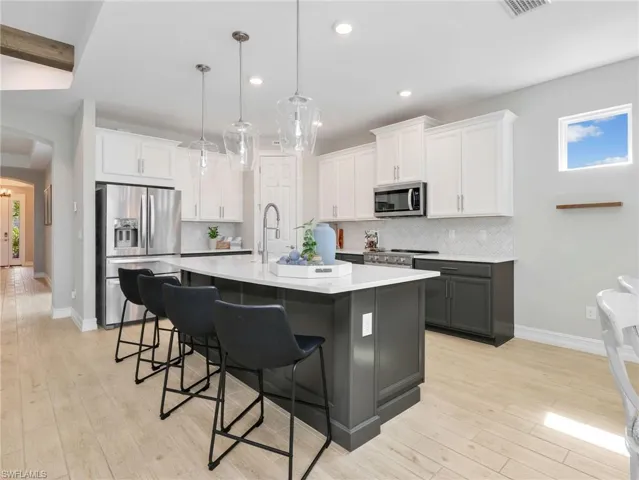 Kitchen featuring a central island with countertop seating, stainless steel appliances, two-tone cabinetry, wood-finish flooring, and pendant lighting