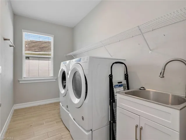 Laundry room featuring wood-finish tile flooring, a window with blinds, and a utility sink with a cabinet base