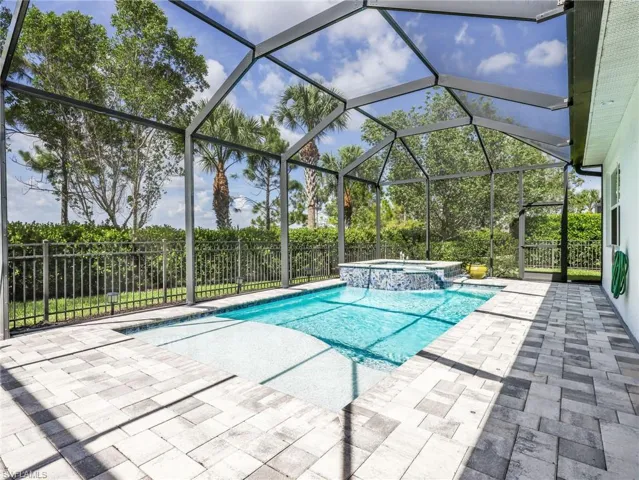 Screened enclosure featuring a swimming pool with integrated spa, paver patio, and surrounding landscaping