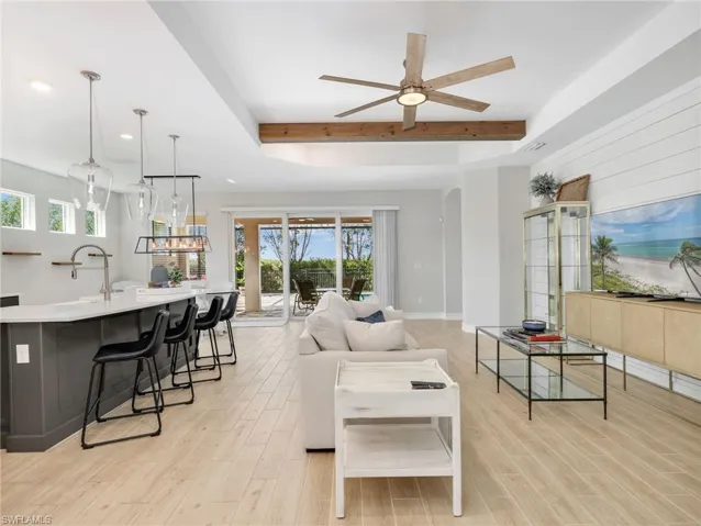 Open-concept living area featuring light wood-finish flooring, a contemporary ceiling fan, and a wood beam accent