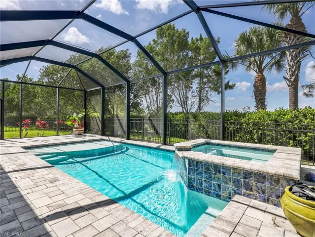 Screened enclosure featuring a rectangular pool, integrated spa with a waterfall feature, and paver decking