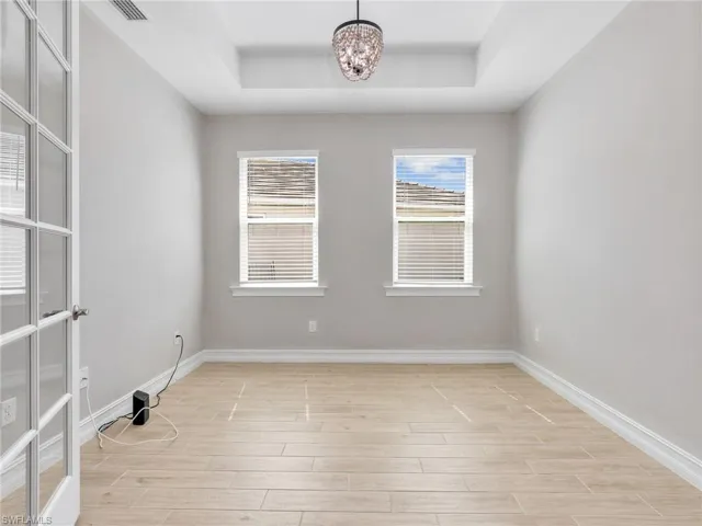 Recessed ceiling with a modern chandelier, two windows with blinds, wood-finish flooring, and a French door entrance