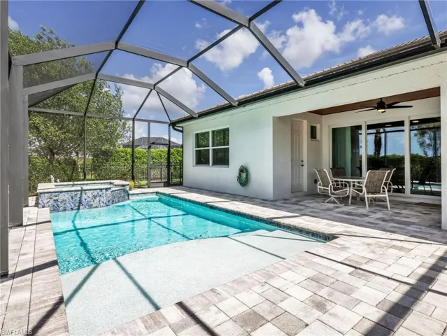 Screened lanai featuring a swimming pool, integrated spa with mosaic tile detailing, and a spacious paver deck
