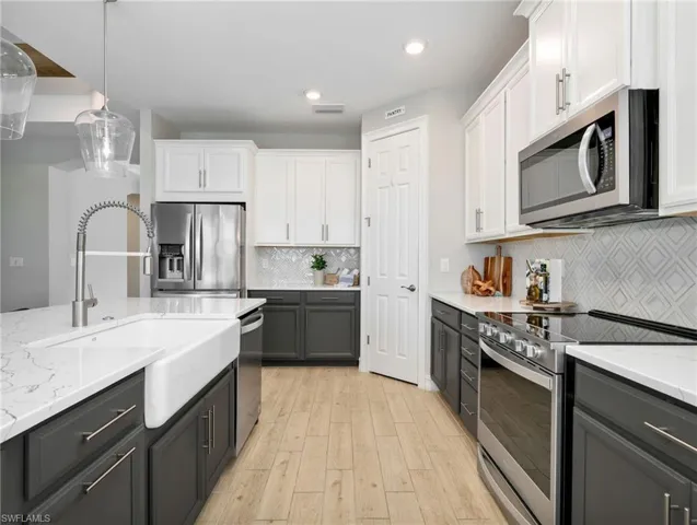Gourmet kitchen featuring a large island with a farmhouse sink, stainless steel appliances, two-tone cabinetry, wood-finish flooring, and a patterned tile backsplash