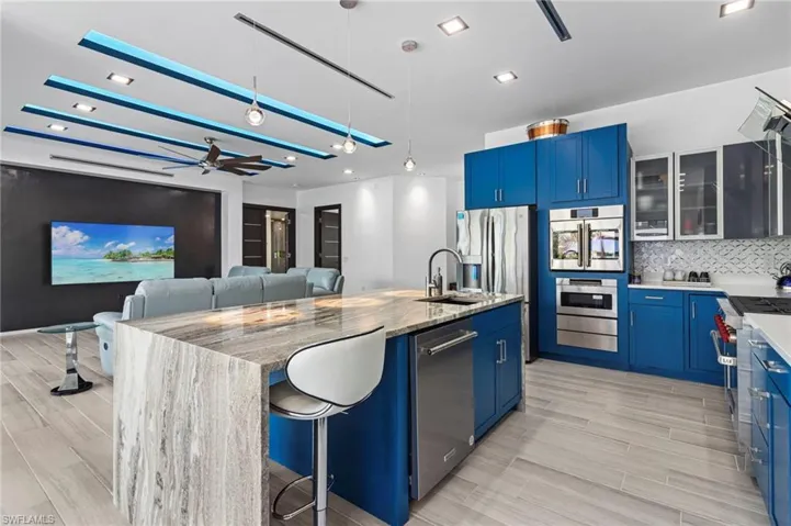 Kitchen with a kitchen island with sink, blue cabinetry, a breakfast bar area, light stone countertops, and decorative backsplash