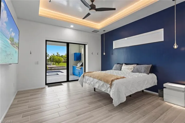 Bedroom featuring light wood-type flooring, a tray ceiling, ceiling fan, and access to exterior