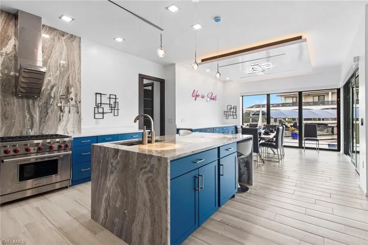 Kitchen featuring pendant lighting, a kitchen island with sink, light stone countertops, luxury stove, and blue cabinetry