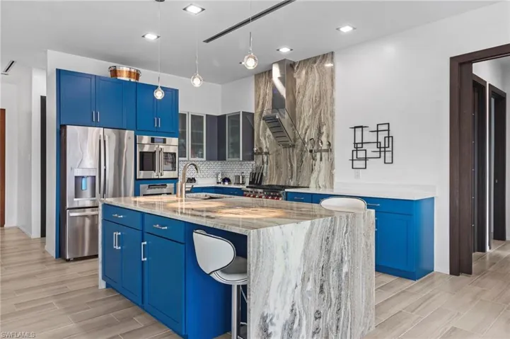 Kitchen featuring sink, a center island with sink, wall chimney exhaust hood, stainless steel appliances, and light stone countertops