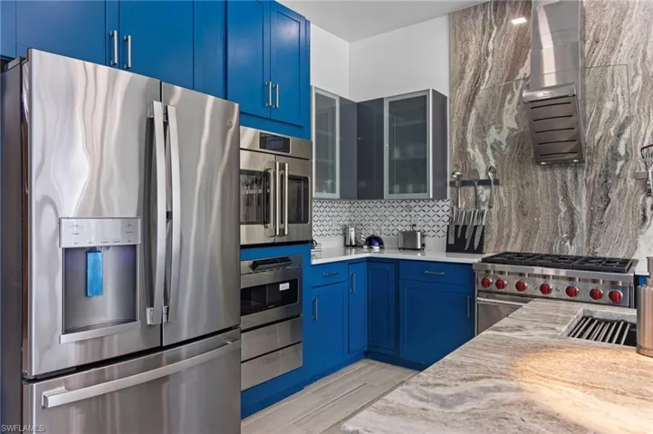 Kitchen with light stone counters, tasteful backsplash, light hardwood / wood-style flooring, stainless steel appliances, and blue cabinetry