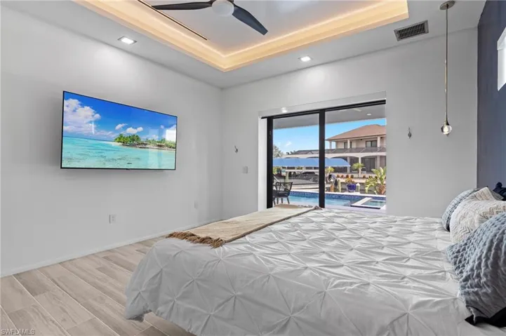 Bedroom featuring ceiling fan, a raised ceiling, hardwood / wood-style floors, and access to exterior
