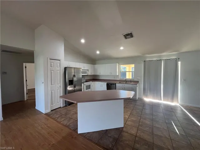Kitchen featuring a kitchen island, white cabinetry, stainless steel appliances, recessed lighting, and high vaulted ceiling