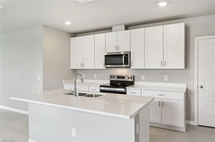 Kitchen with stainless steel appliances, a sink, a center island with sink, white cabinets, and light countertops