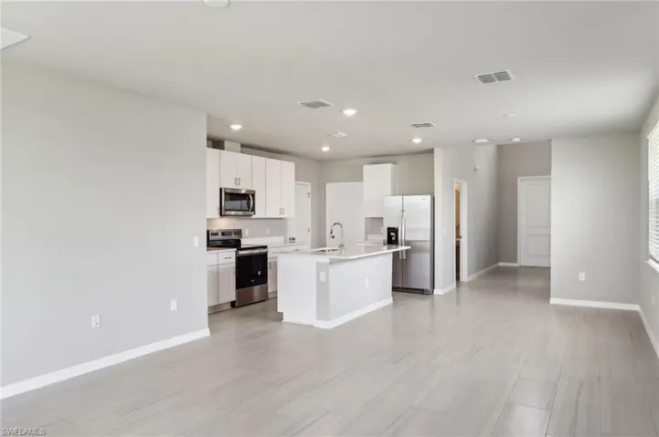 Kitchen featuring appliances with stainless steel finishes, a sink, a center island with sink, baseboards, and white cabinets