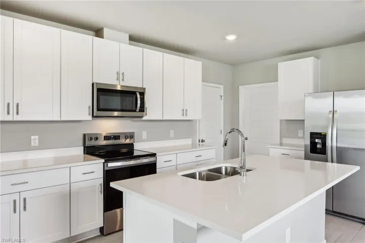 Kitchen featuring appliances with stainless steel finishes, a sink, light countertops, a center island with sink, and white cabinetry