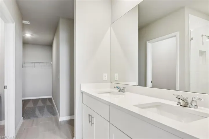 Full bathroom with double vanity, a spacious closet, a shower, and baseboards