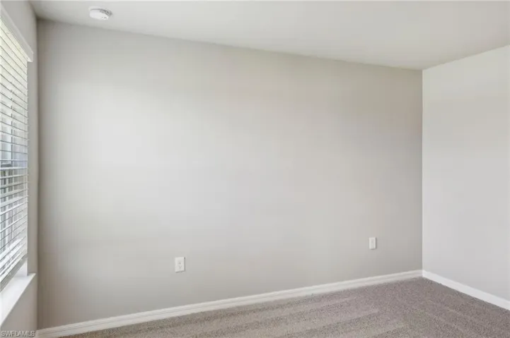 Carpeted spare room featuring a smoke detector and baseboards