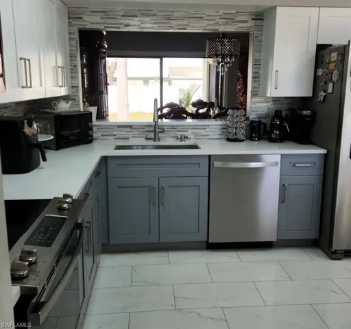 Kitchen with sink, dishwasher, backsplash, and light tile floors