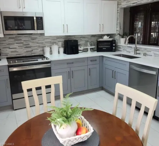 Kitchen with tasteful backsplash, stainless steel appliances, light tile flooring, sink, and white cabinetry