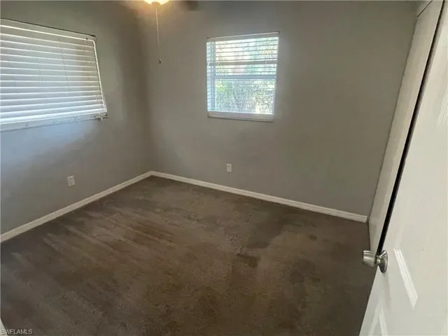 Unfurnished room with dark colored carpet and baseboards