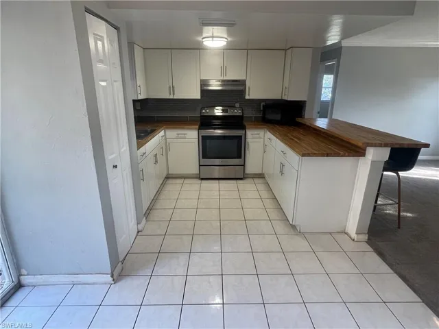 Kitchen featuring electric range, backsplash, butcher block counters, white cabinets, and light tile patterned floors