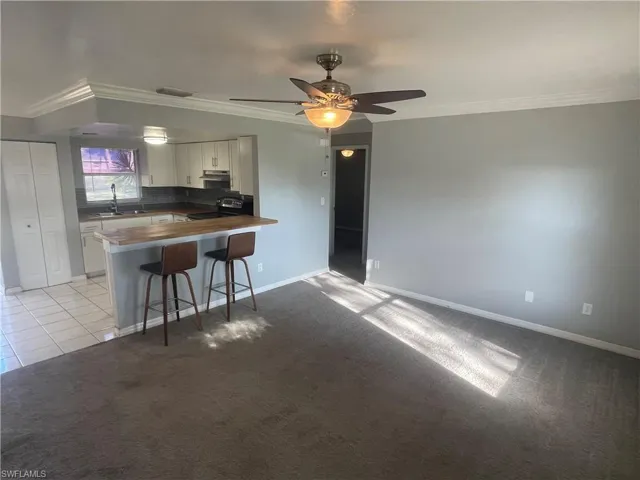 Kitchen with ornamental molding, light colored carpet, white cabinetry, a breakfast bar, and a peninsula