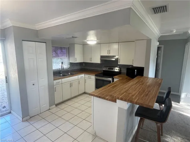 Kitchen with crown molding, butcher block countertops, a kitchen bar, backsplash, and white cabinetry
