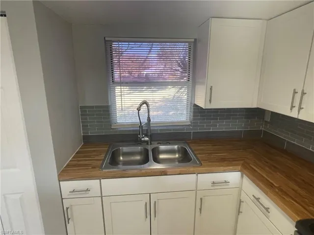 Kitchen with white cabinetry, backsplash, and wood counters