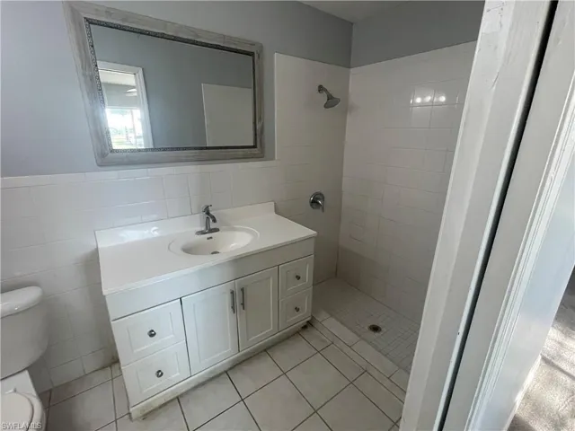 Full bathroom with tile walls, vanity, a shower stall, and light tile patterned floors