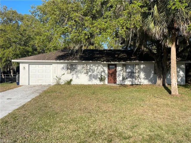 Ranch-style house with stucco siding, a front yard, concrete driveway, a shingled roof, and a garage