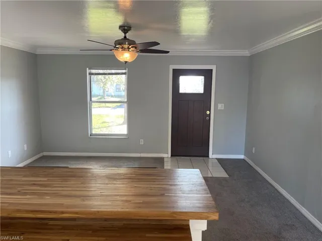 Carpeted entryway featuring ornamental molding, ceiling fan, and wood finished floors
