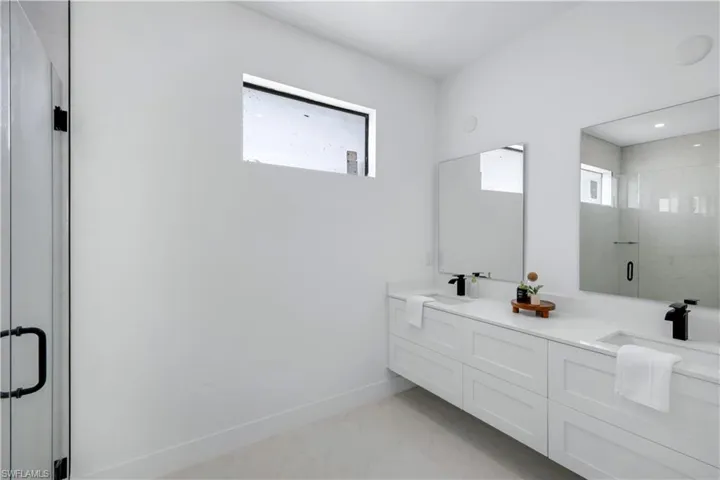 Full bath with healthy amount of natural light, a stall shower, double vanity, and baseboards